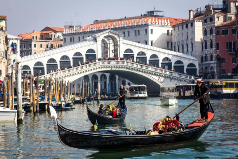 a group of boats in a canal with Rialto Bridge in the background